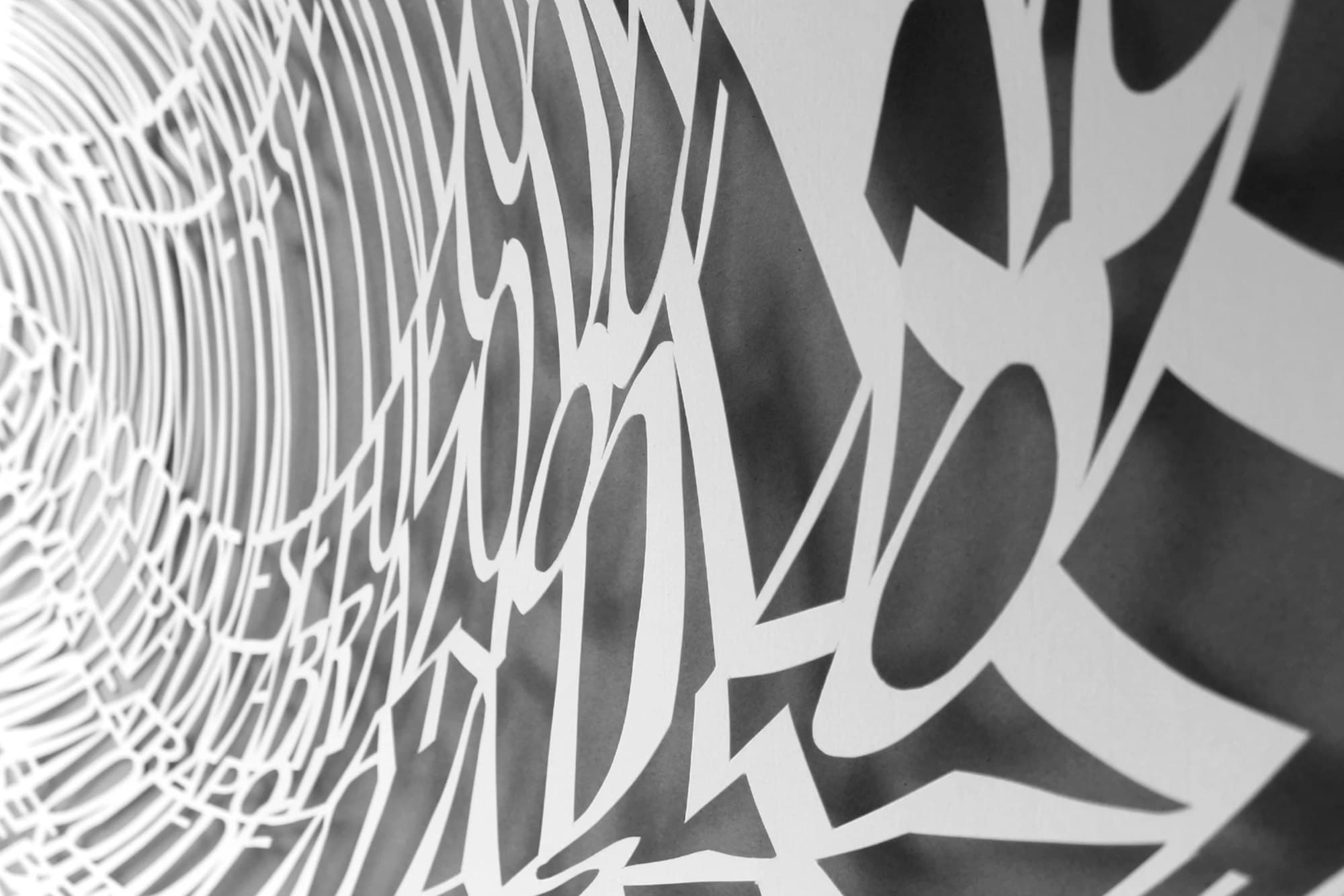 Detalle de papel blanco calado: letras en espiral y su sombra