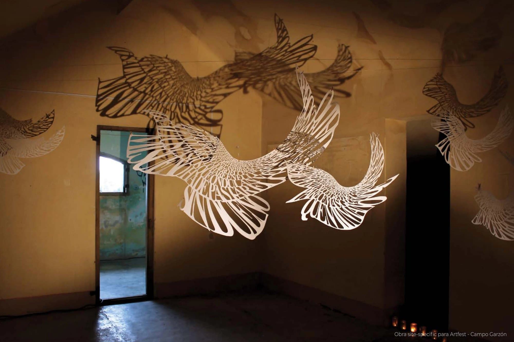 Templum: pájaros de papel calado suspendidos, con sus sombras en la pared