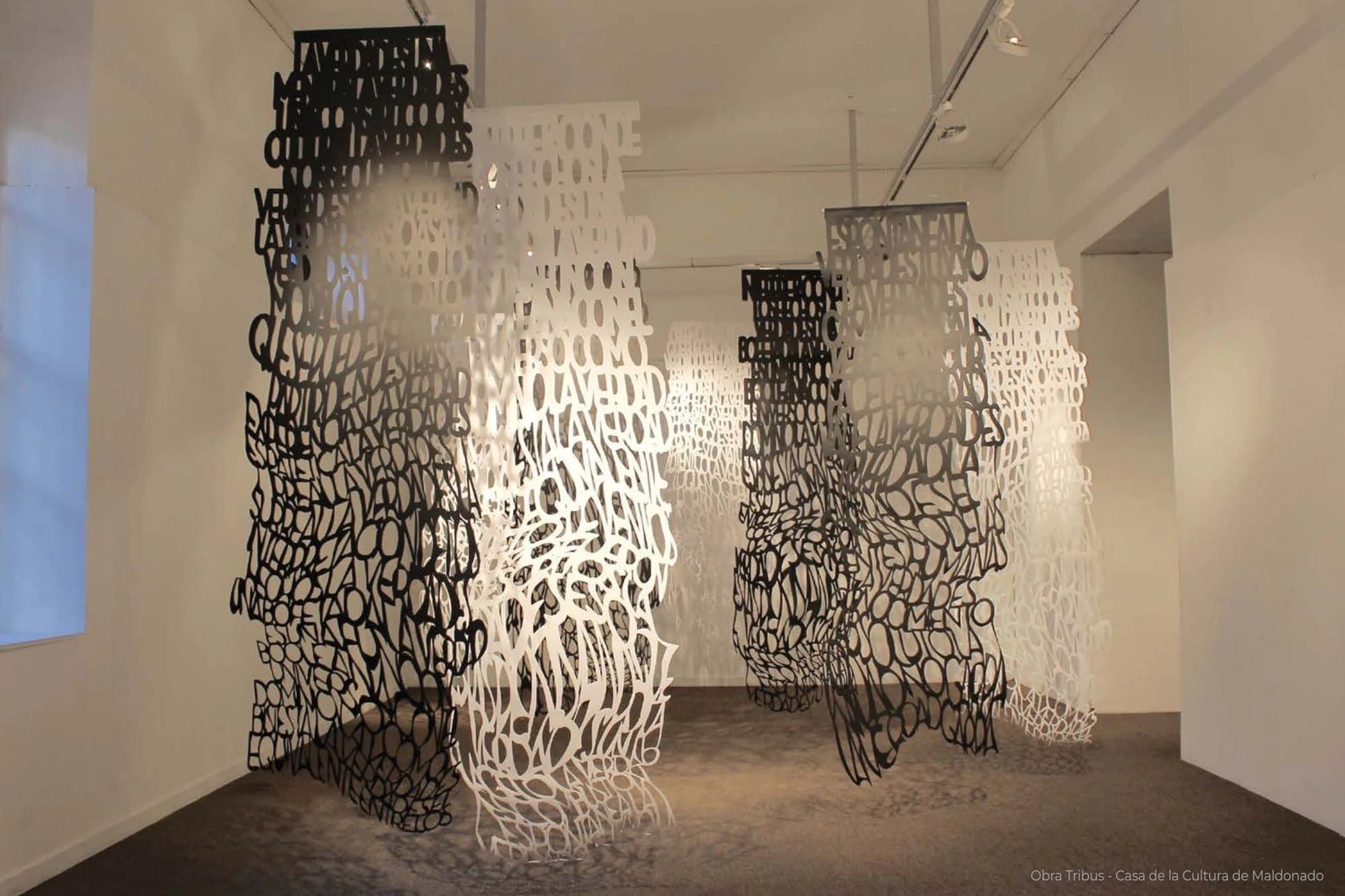 Tribus: columnas de papel calado blanco y negro colgadas en una sala